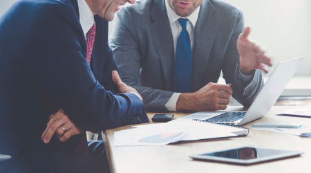 Men in suits discussing business by laptop