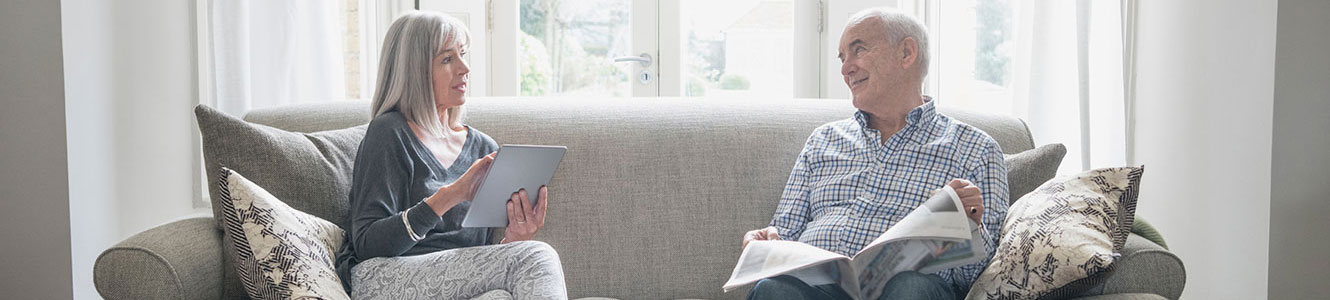 Senior couple at home reading paper and on tablet