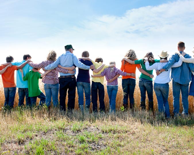 Group of people standing with arms around each other in a field 