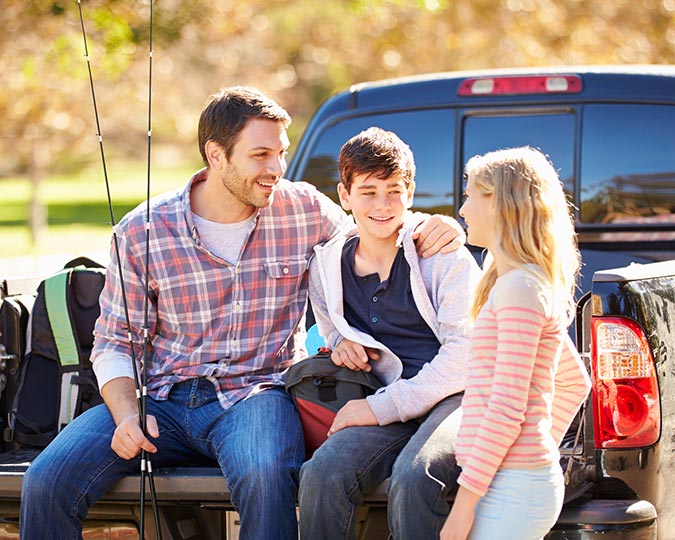 Family sitting in the bed of a truck with fishing poles, preparing to go fishing