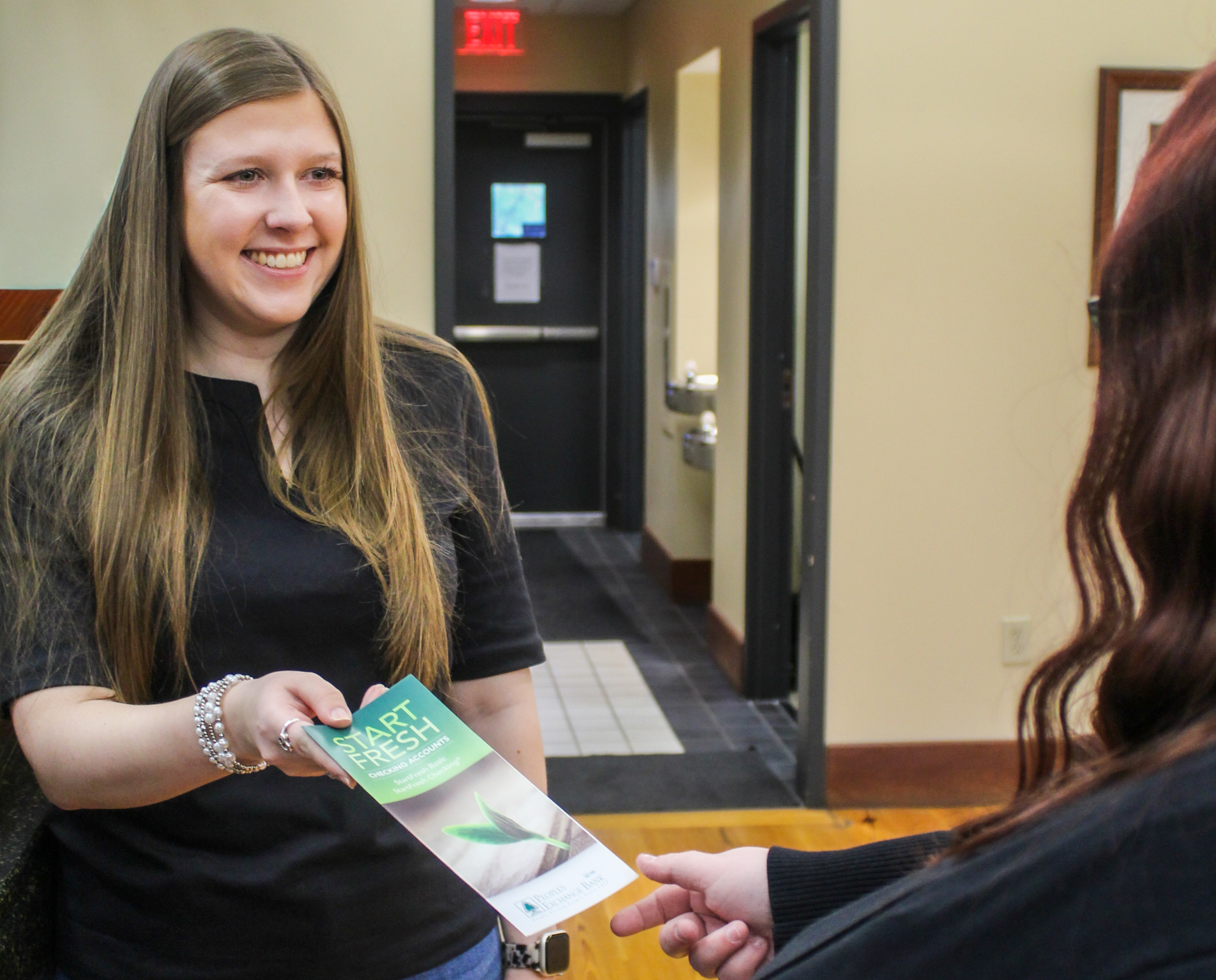 Peoples Exchange Bank employee smiling while handing a client a Start Fresh Account brochure